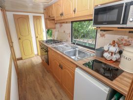 A narrow kitchen with wooden cabinets a sink stove microwave and a window at Lazy Trout Caravan Ludchurch near Narberth
