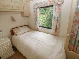 A small bedroom with a single bed a nightstand and a window with floral curtains at Lazy Trout Caravan Ludchurch near Narberth