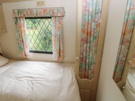 A bedroom with a bed covered by a white bedspread a window with floral curtains and a mirrored closet door at Lazy Trout Caravan Ludchurch near Narberth