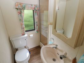A bathroom with a toilet sink mirror and window with floral curtains at Lazy Trout Caravan Ludchurch near Narberth