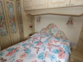 A bedroom with a bed with floral bedding and built-in wardrobes at Lazy Trout Caravan in Ludchurch near Narberth