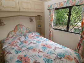 A bedroom with a floral patterned bedspread and matching curtains next to a window with lattice design at Lazy Trout Caravan Ludchurch near Narberth