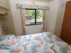 A bedroom with bed covered in floral and bird patterned bedding and window with floral curtains at Lazy Trout Caravan Ludchurch near Narberth