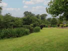 A grassy area next to a pond with trees and shrubs at Lazy Trout Caravan Ludchurch near Narberth