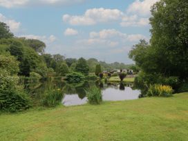 A pond surrounded by grass and trees with buildings in the background at Lazy Trout Caravan Ludchurch near Narberth