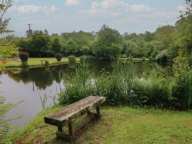 A pond surrounded by trees and grass with a wooden bench in the foreground at Lazy Trout Caravan Ludchurch near Narberth