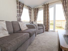 A living room with a sofa and armchair with cushions curtains on windows and a glass door leading outside at 31 Forest Views Moota near Aspatria