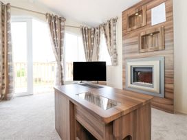 A living room with a wooden coffee table a flat screen tv curtains and a wall-mounted electric fireplace at 31 Forest Views in Moota near Aspatria