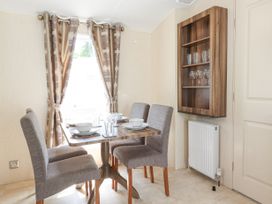 A dining area with a wooden table set for four and four upholstered chairs near a window with patterned curtains at 31 Forest Views in Moota near Aspatria
