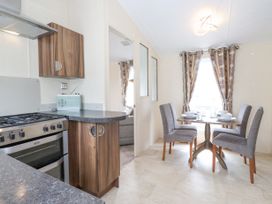 A kitchen area with a stove and wooden cabinets next to a dining table with four gray chairs set with bowls and glasses at 31 Forest Views in Moota near Aspatria