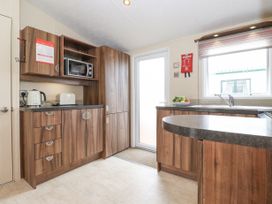 A kitchen with wooden cabinets a microwave a toaster a kettle a bowl of fruit a sink and a door with a window at 31 Forest Views in Moota near Aspatria