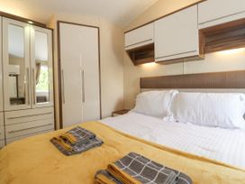 A bedroom with a double bed with pillows and folded towels on a yellow blanket and wardrobes with mirrors at 31 Forest Views in Moota near Aspatria