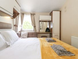 A bedroom with a bed yellow blanket and folded towels a window with curtains and a dressing table at 31 Forest Views in Moota near Aspatria
