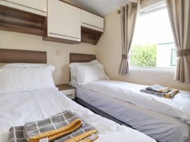 A bedroom with two single beds white bedding towels on beds and a window with curtains at 31 Forest Views in Moota near Aspatria