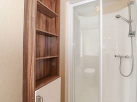 A bathroom with a shower enclosure and a wooden shelving unit with white cabinet door at 31 Forest Views Moota near Aspatria