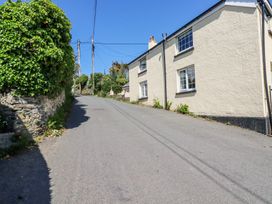 A narrow paved road with a cream house on the right and a stone wall covered with greenery on the left at Hilldene Treknow