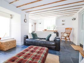 A living room with a black sofa with pillows a plaid ottoman a wooden chair and window at Hilldene in Treknow