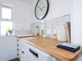 A kitchen counter with a wooden countertop a white sink gold faucet a large wall clock and kitchen accessories at Hilldene in Treknow