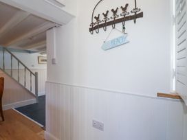 A hallway with white paneled walls a staircase and a wall hook with a beach sign at Hilldene in Treknow