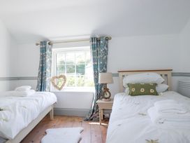 A bedroom with two single beds a window with curtains a bedside table and a lamp at Hilldene in Treknow