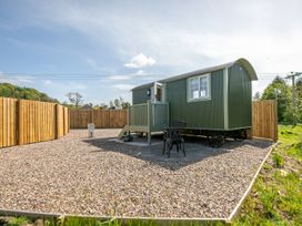 A small green tiny house on wheels with a fenced gravel yard and two black chairs at Strathmore in Burnside near Forfar