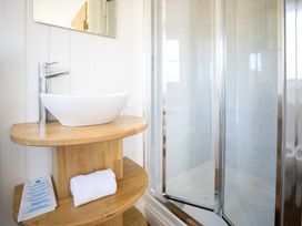 A bathroom with a wooden vanity holding a white sink and a folded towel next to a glass shower enclosure at Strathmore in Burnside near Forfar