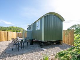 A small green cabin on wheels with a round patio table and two chairs outside surrounded by a wooden fence at Strathmore Burnside near Forfar