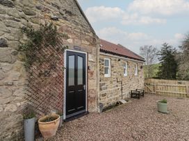 An outdoor entrance with a black door and stone wall at Honeysuckle Cottage in Crookham near Cornhill-On-Tweed