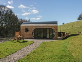 A small wooden cabin with large glass doors and a picnic table on grass at Longlands Lodge Longlands near Caldbeck