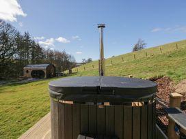 A hot tub with a chimney outdoors on grass with a wooden cabin in the background at Longlands Lodge in Longlands near Caldbeck