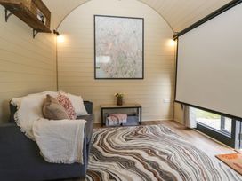 A small living room with a couch with cushions and a throw blanket a patterned rug a wall-mounted shelf a framed map on the wall a table with a vase of flowers and storage baskets and a window with a pull-down screen at Longlands Lodge Longlands near Caldbeck