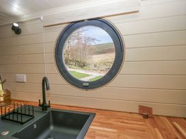 A kitchen sink with a black faucet under a round window showing an outdoor landscape at Longlands Lodge in Longlands near Caldbeck