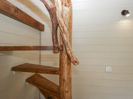A wooden spiral staircase with natural wood handrail and steps inside a room with white paneled walls at Longlands Lodge Longlands near Caldbeck