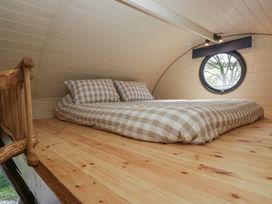 A loft bedroom with a mattress and checked bedding near a round window at Longlands Lodge in Longlands near Caldbeck