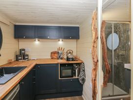A kitchen with dark cabinets wooden countertops a kettle knife set sink and a shower visible through an open door at Longlands Lodge in Longlands near Caldbeck