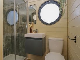 A bathroom with a shower cabin a sink with cabinet a round window and a toilet at Longlands Lodge in Longlands near Caldbeck