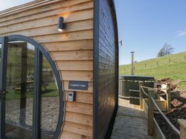 The exterior corner of a wooden lodge with a circular glass door and an outdoor hot tub on a wooden deck at Longlands Lodge Longlands near Caldbeck