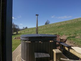An outdoor hot tub with wooden steps on a wooden deck with a grassy hill in the background at Longlands Lodge in Longlands near Caldbeck