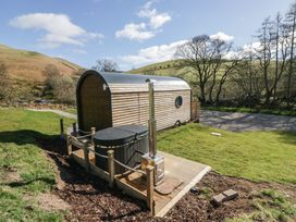 A small wooden cabin with a hot tub on a deck in a grassy outdoor area at Longlands Lodge in Longlands near Caldbeck