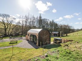 Two wooden pod cabins on grassy land with trees in the background and a picnic table to the left at Longlands Lodge in Longlands near Caldbeck