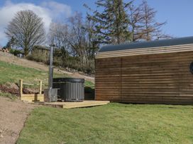 An outdoor wooden hot tub with a metal chimney next to a curved wooden cabin at Longlands Lodge in Longlands near Caldbeck