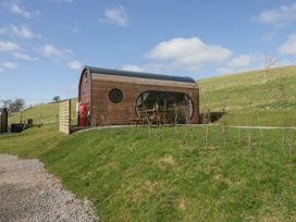 A small wooden cabin with oval windows on a grassy hill at Longlands Lodge in Longlands near Caldbeck
