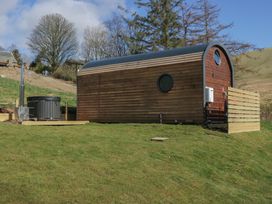 A wooden cabin with a circular window and a hot tub on a grassy slope at Longlands Lodge in Longlands near Caldbeck