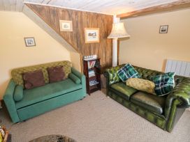 A living room with green and brown sofas and a bookshelf at 2 Strand Cottages in Laugharne