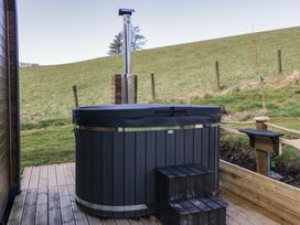 An outdoor hot tub with a chimney and steps on a wooden deck next to a grassy hillside at Binsey Lodge in Longlands near Caldbeck