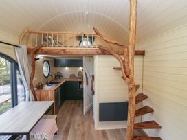 An interior of a small wooden cabin with a loft bed above a kitchen area and wooden spiral stairs at Binsey Lodge in Longlands near Caldbeck