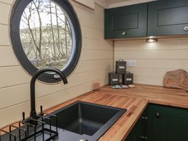 A kitchen corner with black sink and faucet under round window with wooden countertop and dark green cabinets at Binsey Lodge in Longlands near Caldbeck