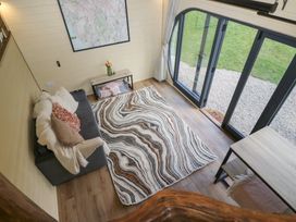 A small living area with a sofa with cushions a patterned rug a table with flowers a framed map on the wall and large glass doors leading outside at Binsey Lodge in Longlands near Caldbeck