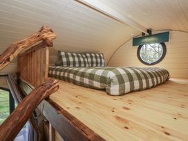 A loft bed with green and white checkered bedding in a small wooden room with a circular window at Binsey Lodge in Longlands near Caldbeck