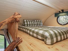 A loft bed with green and white checkered bedding and a wooden railing with a round window in the background at Binsey Lodge in Longlands near Caldbeck
